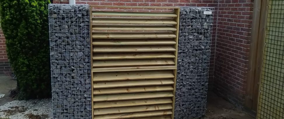 Schanskorfzuilen zijn veelzijdig te gebruiken in uw tuinontwerp. Twee schanskorfzuilen met ertussen een houten deur ter afscheidingswand voor de containers.