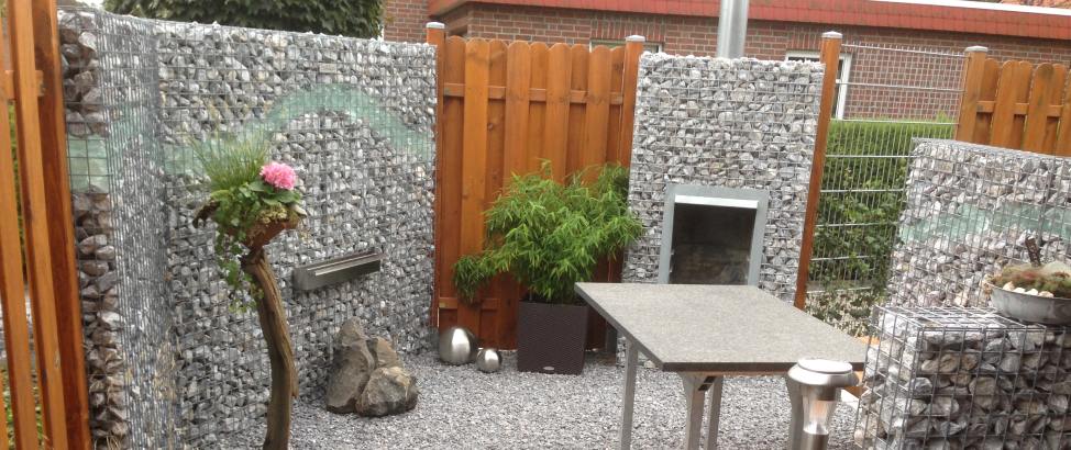 Tuin met schanskorven gecombineerd met houten tuinschermen, inclusief haard, planten en decoratie