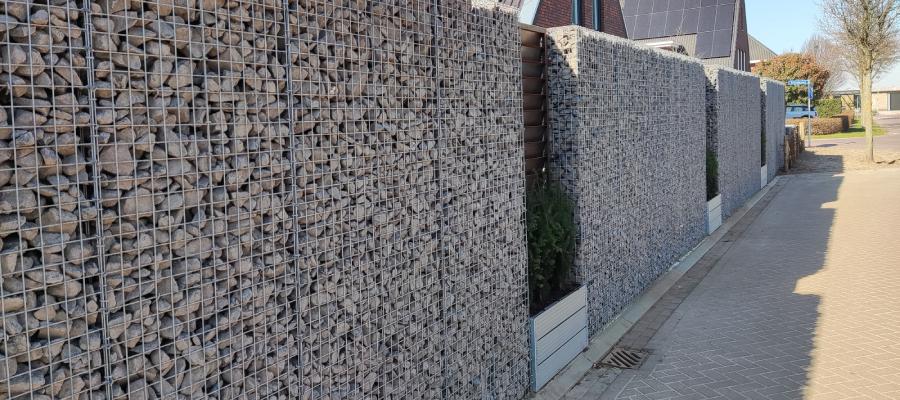 Geniet van rust, privacy en geef uw tuin een robuuste uitstraling met Gabion Schanskorven Schutting van schanskorven gevuld met breukstenen in een woonwijk.
